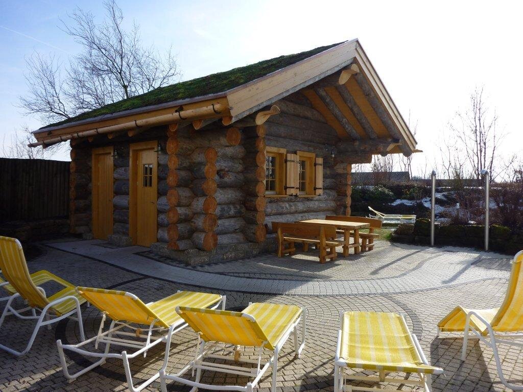 Das Bild zeigt ein Holzhaus von der Seite, im Vordergrund stehen gelbe Liegestühle.