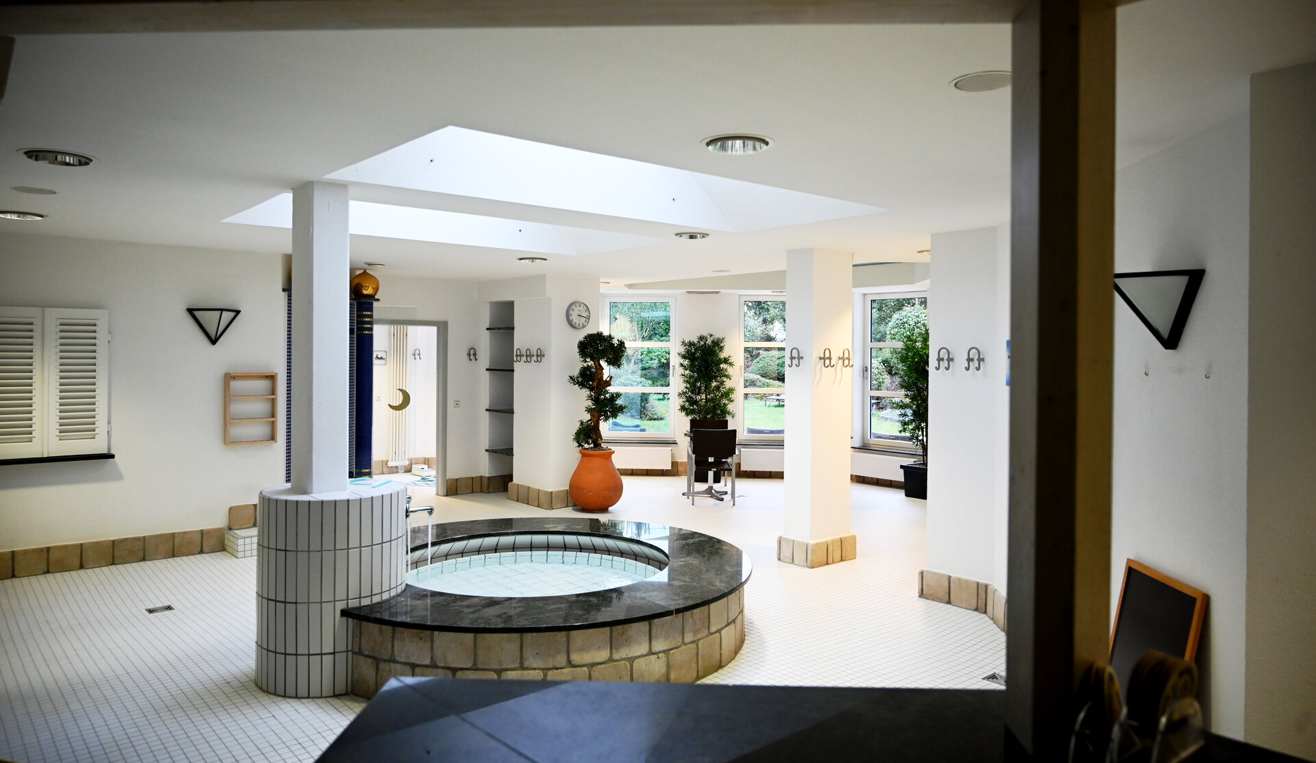Das Bild zeigt einen hellen Innenraum mit einem kleinen Brunnen in der Mitte.