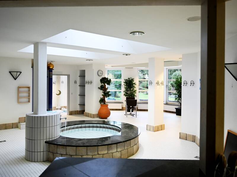 Das Bild zeigt einen hellen Innenraum mit einem kleinen Brunnen in der Mitte.