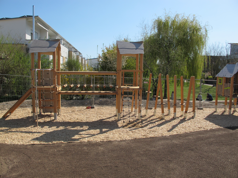 Ein Spielplatz mit verschiedenen Holzklettergerüsten und Balancierbalken auf einem mit Holzschnitzeln bedeckten Boden.