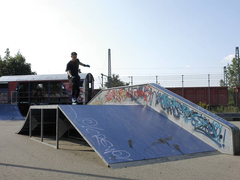 Eine Person fährt mit Skates über eine Rampe in einem Skatepark, der mit Graffiti verziert ist.