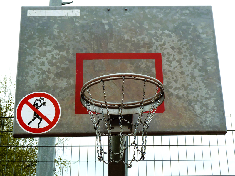 Ein Basketballkorb aus Metall mit einem Verbotsschild, das das Slam-Dunken untersagt, ist an einem Gitterzaun montiert.