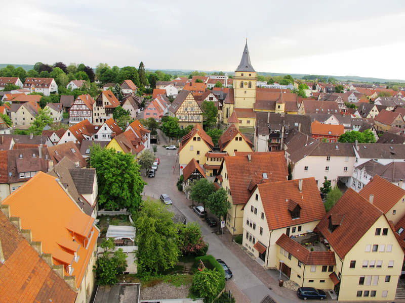 Eine malerische Kleinstadt mit zahlreichen roten Ziegeldächern, Fachwerkhäusern, einer Kirche und umgeben von vielen Bäumen.