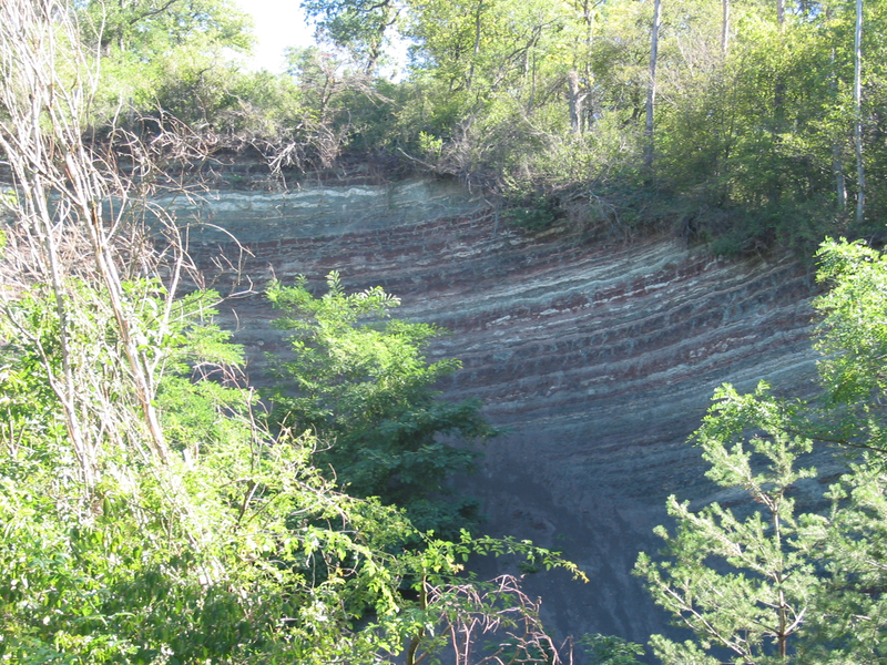 Eine steile, bewaldete Felswand mit sichtbaren geologischen Schichtungen und üppigem Grün erhebend darüber.