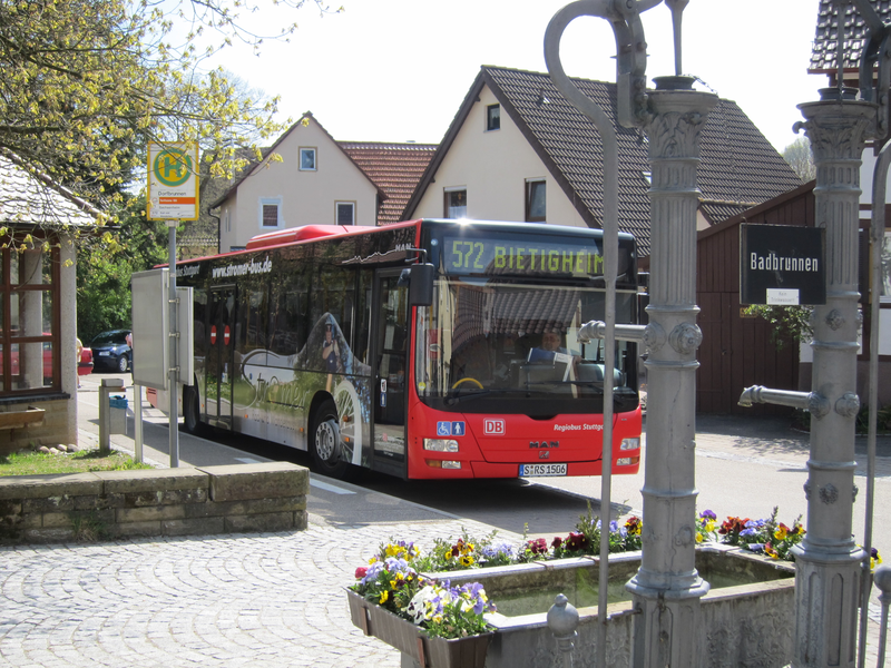 Ein roter Linienbus mit der Aufschrift "572 Bietigheim" steht an einer Haltestelle vor einem Gebäude in einer ländlichen Umgebung.