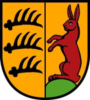 Das Bild zeigt ein Wappen mit drei schwarzen Hirschstangen auf gelbem Grund links und einem aufrechten roten Hasen auf grünem Hügel rechts.