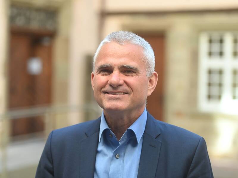 Bürgermeister Holger Albrich steht in einem dunkelblauen Anzug vor einem unscharfen Hintergrund mit Gebäuden.